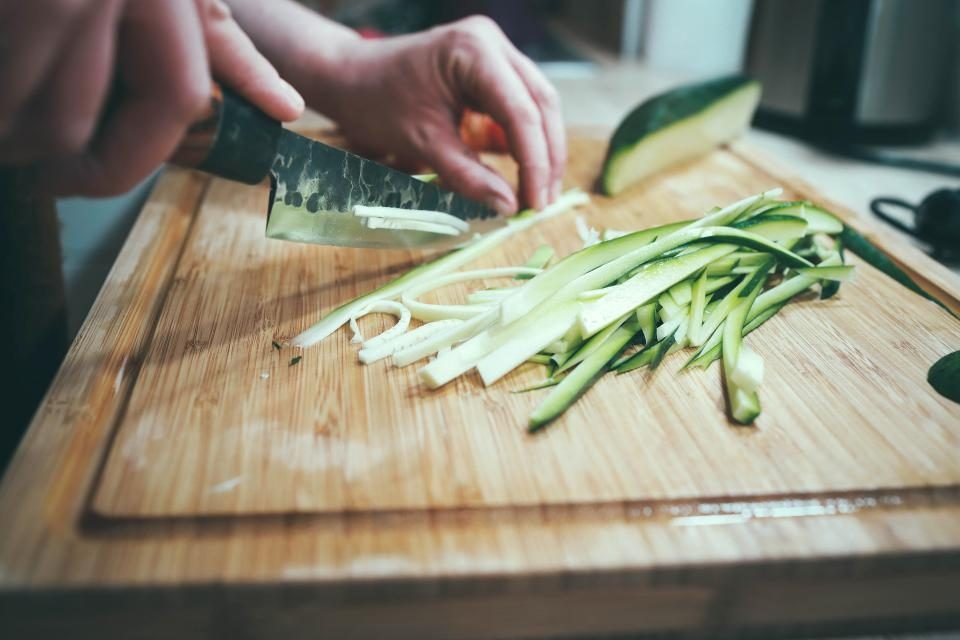 Hands slicing fresh vegetables into thin strips on a wooden chopping board